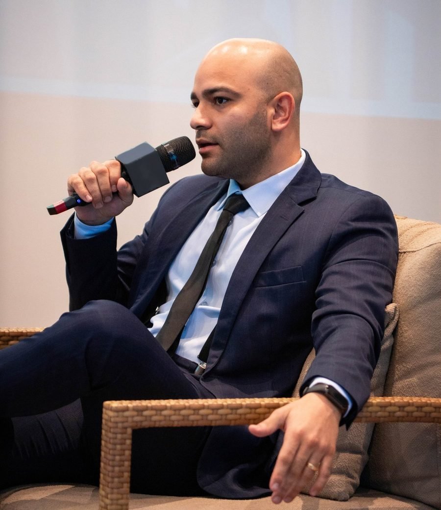 Caio Nascimento falando ao microfone, de perfil